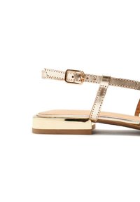 Sandalia con tiras en un acabado metálico rosa dorado, tacón cuadrado plano y un diseño minimalista que presenta una hebilla simple y una textura suave.