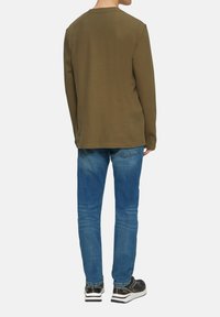 Camisa de manga larga verde oliva con cuello redondo, combinada con jeans de mezclilla azules y zapatillas negras con suelas blancas.