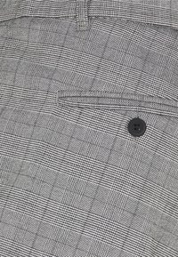 Grått rutmönstrat tyg med ett subtilt rutmönster och en mjuk textur, en enda svart knapp och en liten fickdetalj i weltstil.