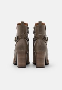 Stivaletti in pelle marrone con tacco in legno impilato, fibbie regolabili sui lati e morbidi dettagli in suede sul retro.