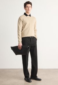 Beige pulóver fekete gallérral, fekete nadrággal és fekete bőr clutch táskával. Sima textúrák, letisztult vonalak és testre szabott fazon.
