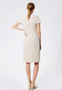 Vestido beige de manga corta con una silueta ajustada, largo hasta la rodilla y costuras sutiles, combinado con tacones de plataforma beige.