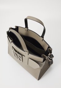 Borsa beige con accenti neri, forma strutturata, manici superiori e dettaglio del logo. L'interno presenta più scomparti e una texture liscia.