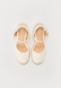 Zapatos de espadrilles blancos con un upper de tela suave, correa lateral en el tobillo, bordado floral decorativo y suelas de yute tejidas de forma natural.