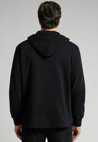 Sudadera negra con capucha ajustable, mangas largas y un corte relajado. Fabricada en un tejido suave con una textura lisa y detalles mínimos.