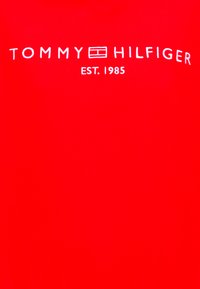 Κόκκινο βαμβακερό ύφασμα με τα λευκά κείμενα "TOMMY HILFIGER" και "EST. 1985". Απλός σχεδιασμός με λεία υφή και χωρίς πρόσθετα γραφικά.