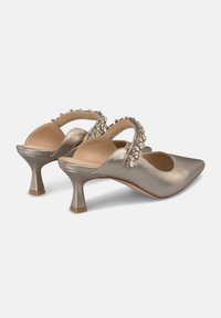 Tacones slingback metálicos en color dorado con punta afilada, que presentan una correa decorativa de cuentas y un tacón corto y curvado. Textura suave.