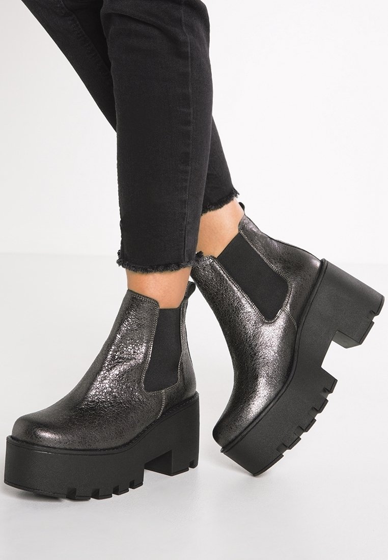 Botas negras hasta el tobillo con un acabado brillante y texturizado, que cuentan con paneles laterales elásticos y una suela de plataforma gruesa con un diseño con relieve.