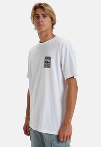 White cotton t-shirt with short sleeves, featuring a chest pocket print of waves and a logo in blue and orange. Plain design, relaxed fit.
