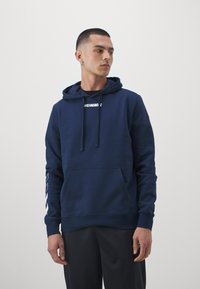 Sweat à capuche bleu marine avec une poche kangourou à l'avant, un cordon de serrage ajustable et un logo blanc sur la poitrine. Tissu texturé avec des manches longues.