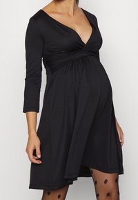 Svart gravidklänning med V-ringning, trekvartsärmar och samlad midja, med ett mjukt, elastiskt tyg och en flödande kjol.