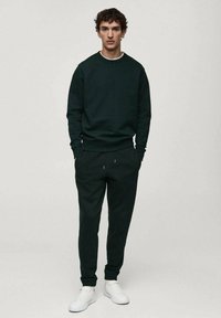 Felpa verde scuro con scollo a girocollo, abbinata a pantaloni jogger coordinati. L'outfit è realizzato in materiale morbido e presenta polsini elasticizzati.