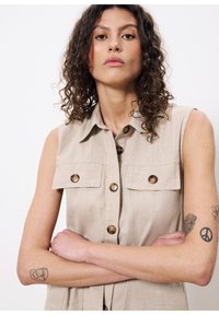 Beiges ärmelloses Kleid mit Knopfleiste, zwei Brusttaschen und einem gerippten Muster. Mit runden Knöpfen und einem spitzen Kragen.