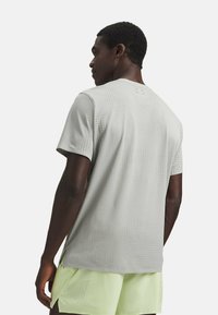 Camiseta atlética de manga corta en gris claro con perforaciones transpirables, cuello redondo y aberturas laterales para ventilación.