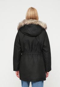 Czarna parka z kapturem wykończonym sztucznym futrem, elastyczną talią, długimi rękawami oraz gładką fakturą. Widok z tyłu pokazuje zaokrąglony dół.