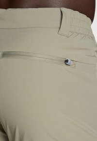 Shorts de randonnée beiges avec une poche zippée dissimulée, une taille élastique et une texture de tissu lisse et léger. Accentué par un onglet de traction rond.