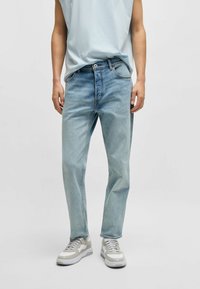 Jasnoniebieskie dżinsy o prostym kroju, pięć kieszeni, szlufki na pasek i kontrastowe szwy. Noszone z neutralnymi sneakersami.