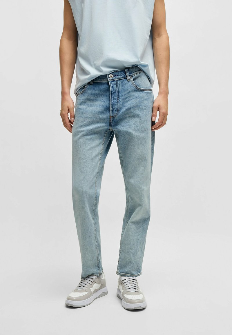 Jasnoniebieskie dżinsy o prostym kroju, pięć kieszeni, szlufki na pasek i kontrastowe szwy. Noszone z neutralnymi sneakersami.