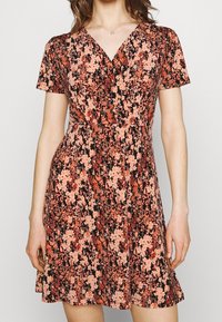 Robe noire à manches courtes avec un motif floral en rose et orange. Présente un décolleté en V et une silhouette évasée en A. Texture de tissu douce.