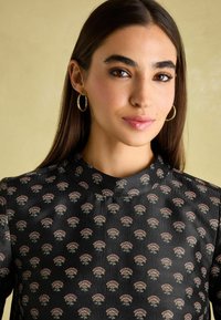 Schwarzstoffoberteil mit einem subtilen Blumenmuster in Rosa- und Grüntönen. Hochgeschnittener Kragen mit sichtbarem Schmuck. Weiche Textur.