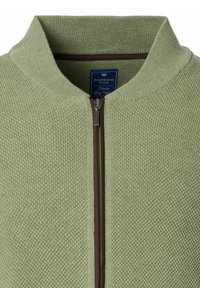 Zielona dzianinowa kurtka na zamek z prążkowanym kołnierzem i brązowym akcentem wzdłuż zamka, wyróżniająca się teksturowanym wzorem oraz metką marki wewnątrz.