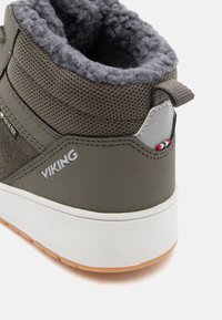 Κοντινή λήψη από μια γκρι-πράσινη βικινγκ μποτάκι με επένδυση από μαλλί, υφασμάτινη υφή, ετικέτα Gore-Tex, λαβή και λευκή σόλα με καφέ πελμά.