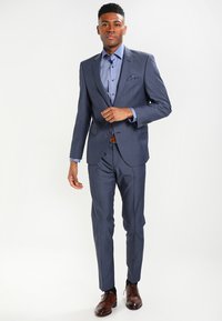 Dark blue suit with a tailored fit, single-breasted jacket, and matching trousers. Accompanied by a light blue shirt and brown leather shoes.