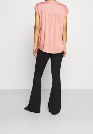 Blusa rosa a maniche corte con dettaglio dei bottoni sul retro, tessuto arricciato sulle spalle, abbinata a pantaloni neri a campana. Texture liscia.