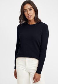Navy strukturierter Strickpullover mit Rundhalsausschnitt und langen Ärmeln, kombiniert mit hellen Jeans. Der Pullover hat einen figurbetonten, lässigen Stil.