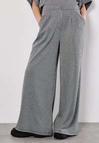 Breda byxor i ett svart och vitt rutmönster. Tillverkade av ett texturerat material med sidofickor och hög midja, matchat med kraftiga svarta skor.