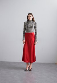 Μακρύ κόκκινο σατέν φόρεμα με στενό καφέ και λευκό ριγέ τοπ με ψηλό λαιμό. Ο σχεδιασμός διαθέτει απαλή υφή και κομψή σιλουέτα.