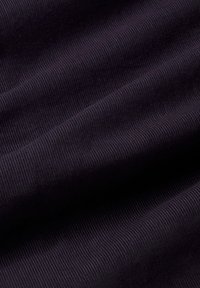 Ciemnofioletowy materiał kordowy o drobnych, pionowych prążkach i miękkich fałdach, tworzący wariacje światła i cienia.