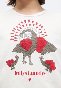 Στυλιζαρισμένο μεγάλο πουλί με απλωμένα φτερά και λεπτομέρειες σε κόκκινο χρώμα, περικυκλωμένο από δύο μικρότερα πουλιά, πάνω από κόκκινο κείμενο «lollys laundry» και μια καρδιά.