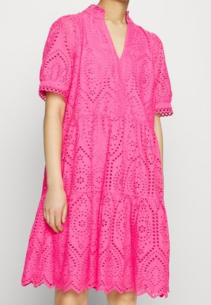 Vrouw die een felroze eyelet kanten jurk draagt met pofmouwen, V-hals, geplooide rok en gekartelde zoom.