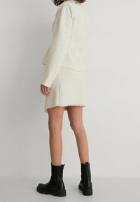 Ensemble deux pièces blanc texturé comprenant une veste courte et une jupe ajustée, accompagnée de bottines noires. Fins bords effilochés sur la jupe.