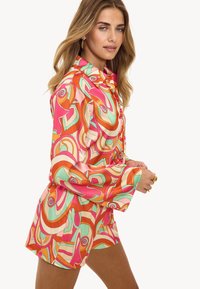 Conjunto de camisa y pantalones cortos de seda multicolor con grandes remolinos abstractos en rosa, naranja y verde. Presenta un cuello y mangas largas.