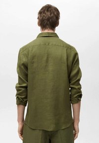 Camicia in lino verde olivo con maniche lunghe, polsini abbottonati e parte posteriore a yoke. L'orlo è leggermente curvato, offrendo una vestibilità rilassata.