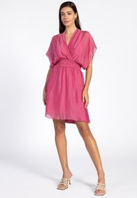 Korte roze jurk met een V-hals, korte mouwen en een gerimpelde taille. Gemaakt van lichte stof, met een vloeiende silhouet.