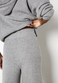 Set di loungewear grigio a maglia con motivo testurizzato, composto da un top morbido e pantaloni a vita alta, che enfatizzano comfort e calore.