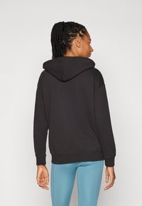 Sudadera negra con capucha y corte relajado, con puños y dobladillo acanalados. Combinada con leggings azul claro, mostrando una textura de tela suave.