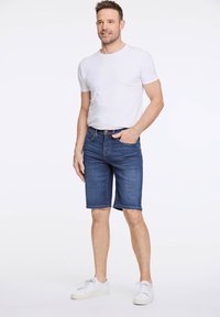 Shorts de denim azul con corte recto y dobladillo. Combinados con una camiseta blanca básica y zapatillas blancas. Diseño clásico con cinco bolsillos.