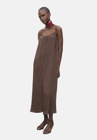 Rochie maxi fără mâneci, de culoare maronie, cu un material texturat, cu legături în față și o croială lejeră, completată cu bretele subțiri și sandale.
