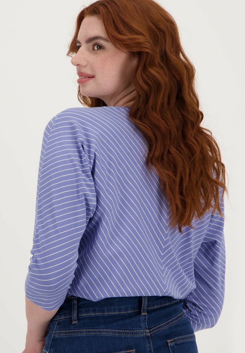 Paarse gestreepte shirt met driekwart mouwen, heeft een chevronpatroon, gemaakt van zachte stof, gedragen met donkerblauwe denimjeans.