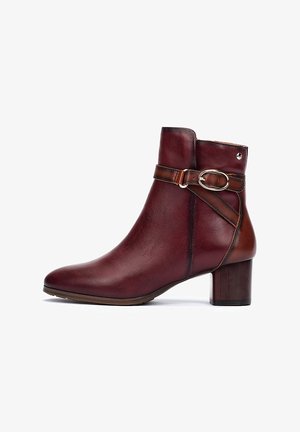 Bottine en cuir bordeaux avec un orteil arrondi, accent brun, boucle décorative et un talon moyen en bloc. Texture lisse et lignes épurées.