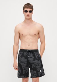 Shorts de bain noirs avec un motif gris semblable à de l'eau, ceinture élastique avec cordon, poches latérales et un petit patch de logo en bas.