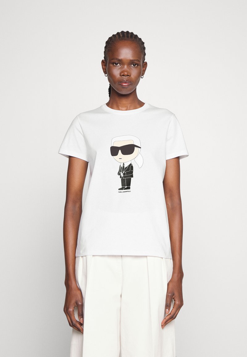 Balta kokvilnas T-krekliņš ar multfilmu attēlu, kurā attēlots tēls saulesbrillēs un melnā uzvalkā, centrā drukāts. Īsas piedurknes, apaļa kakla izgriezums.