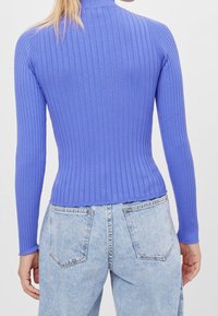 Top de manga larga con cuello alto en morado claro, combinado con jeans de mezclilla de tiro alto en azul claro. La tela es elástica y ajustada.