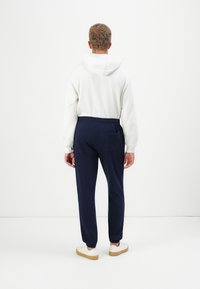 Hvit hettegenser med en avslappet passform, kombinert med marineblå joggebukser med elastisk midje og baklomme; kremfargede joggesko.