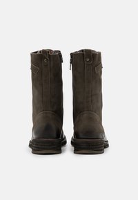 Botas de cuero marrón hasta el tobillo con cierre de cremallera, costuras decorativas y una suela texturizada. Acabadas con un logo en el tacón.