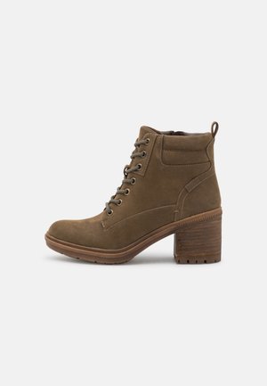 Bottine en daim marron avec lacets à l'avant, col rembourré, languette à tirer et talon épais empilé sur fond blanc.
